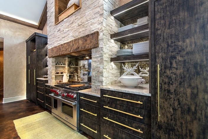 A kitchen with black cabinetry and a stone fireplace above the stove