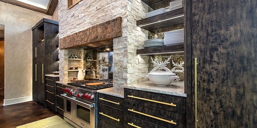A kitchen with black cabinetry and a stone fireplace above the stove