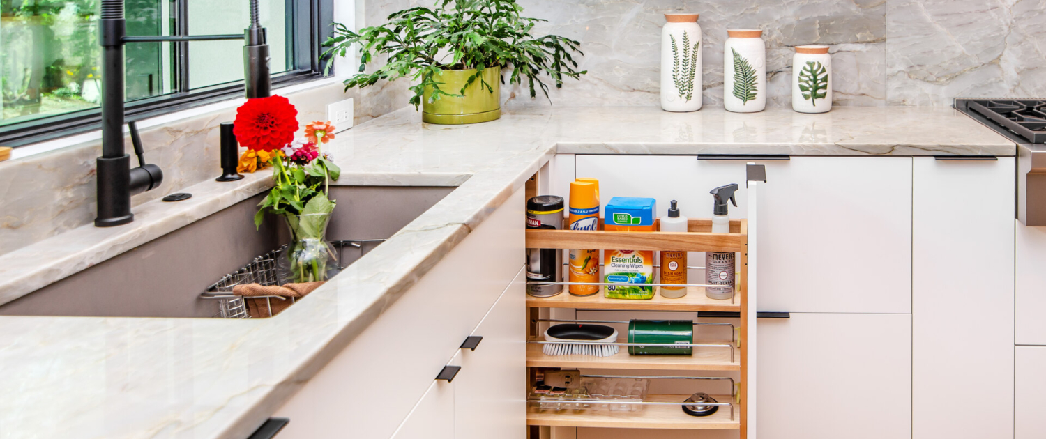 A kitchen with white cabinetry and a pull out drawer open with cleaning supplies all in it