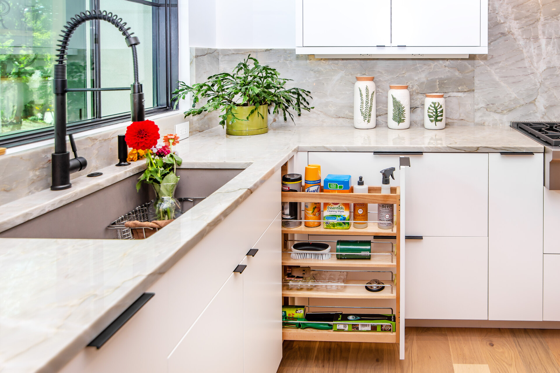 A kitchen with white cabinetry and a pull out drawer open with cleaning supplies all in it