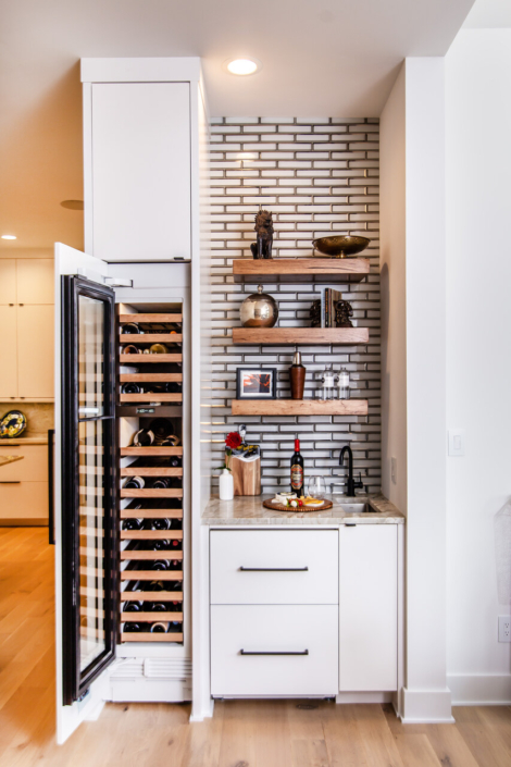 A wet bar with floating shelves and a wine cooler with a paneled door