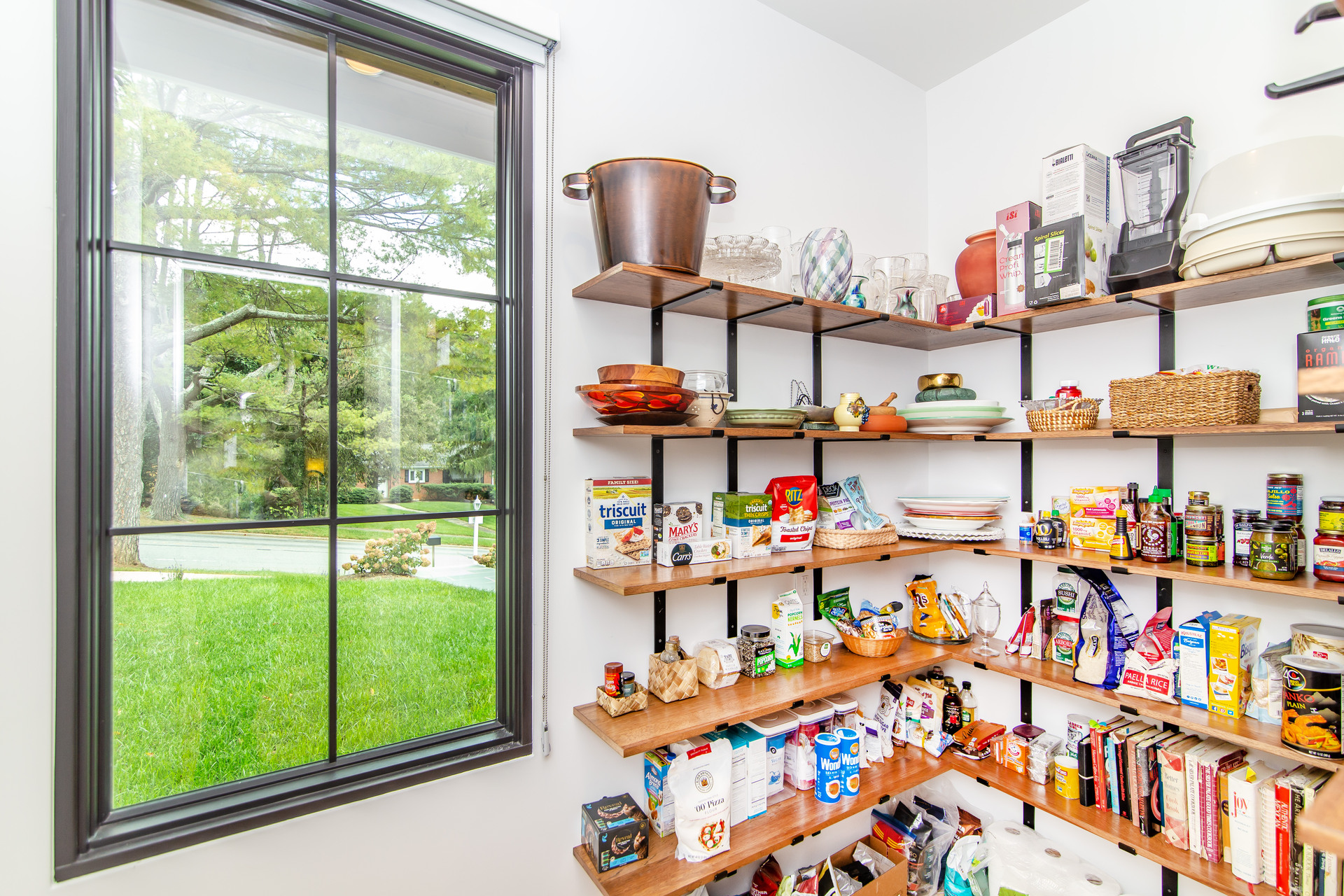 A walk in pantry with walnut open shelving with food all on it and with a large window