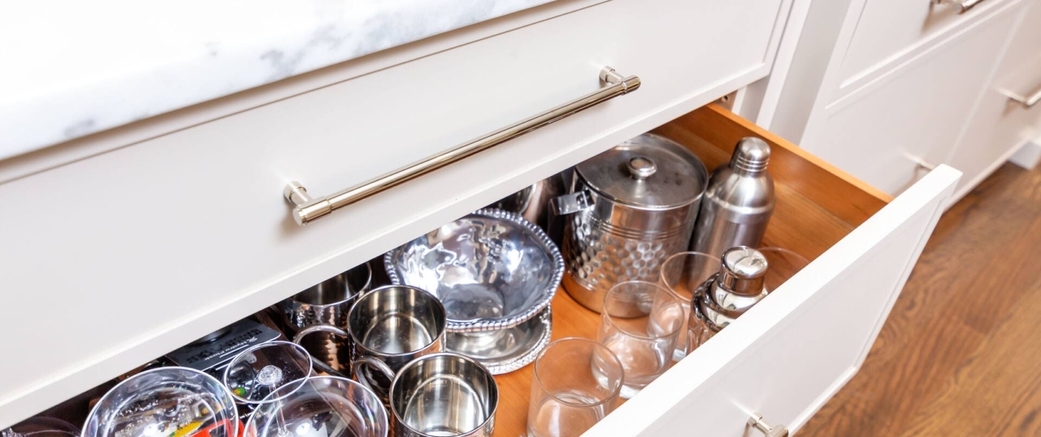 A kitchen with a custom maple deep cabinet drawer for glass storage