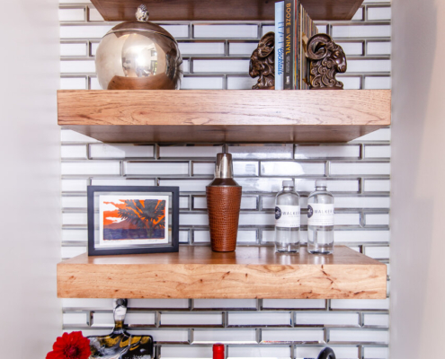 A wet bar with wood floating shelves and decor pieces displayed all on them