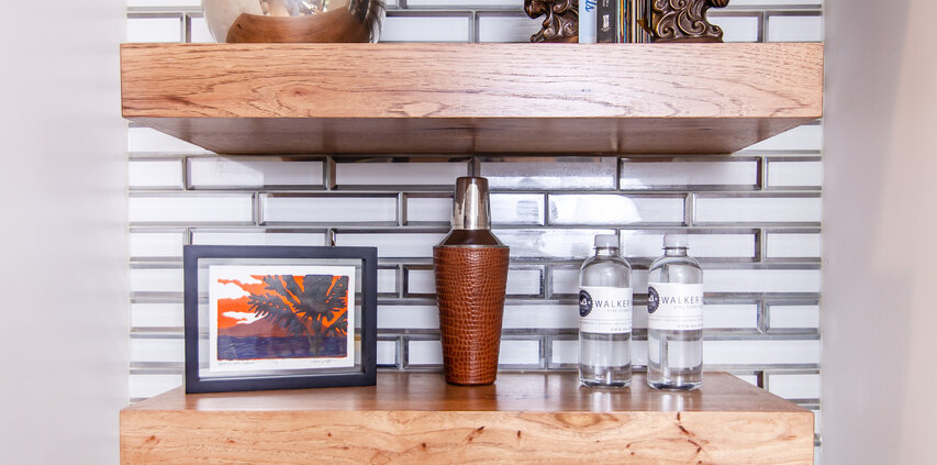 A wet bar with wood floating shelves and decor pieces displayed all on them