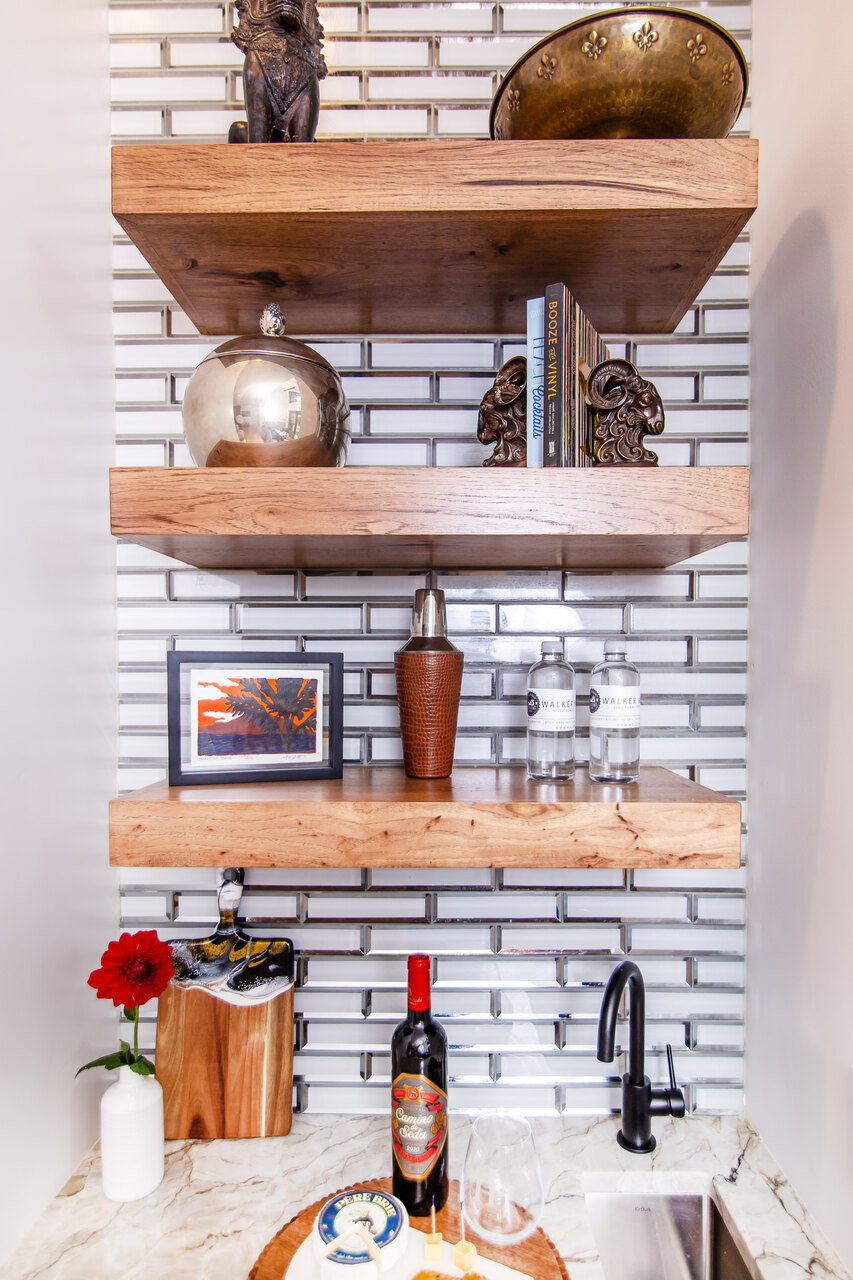 A wet bar with wood floating shelves and decor pieces displayed all on them