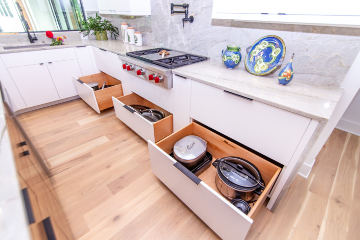 A white kitchen with three deep slab cabinet drawers pulled open with storage