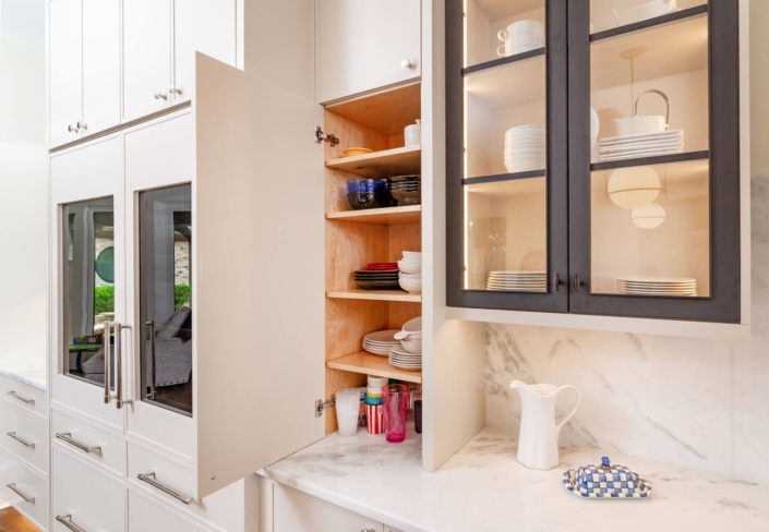 A kitchen with white cabinetry and with black metal glass cabinet doors with lighting inside