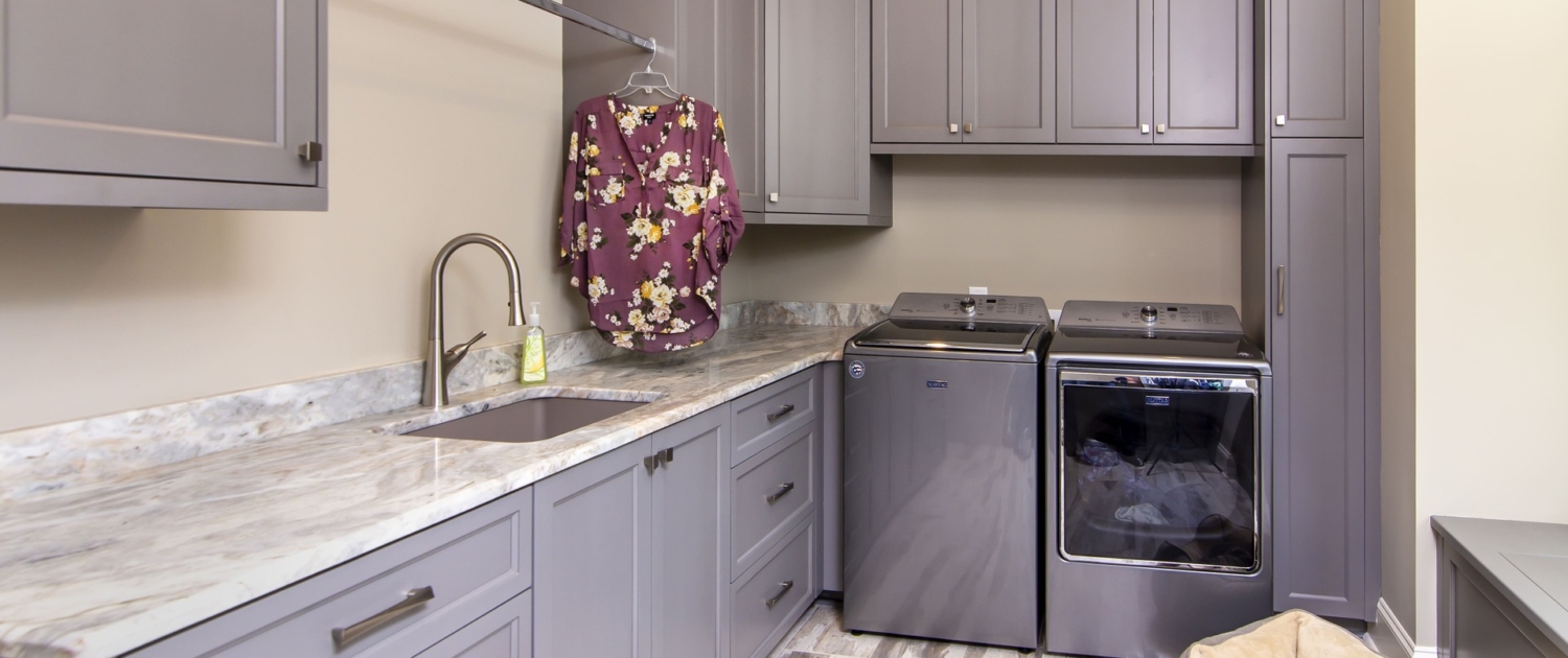 Grey laundry room cabinets with marble countertops