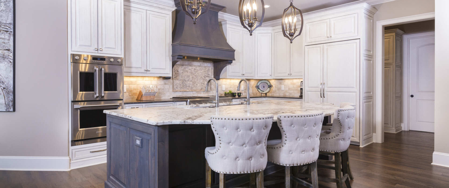 White kitchen cabinets with a brown island and large light fixtures