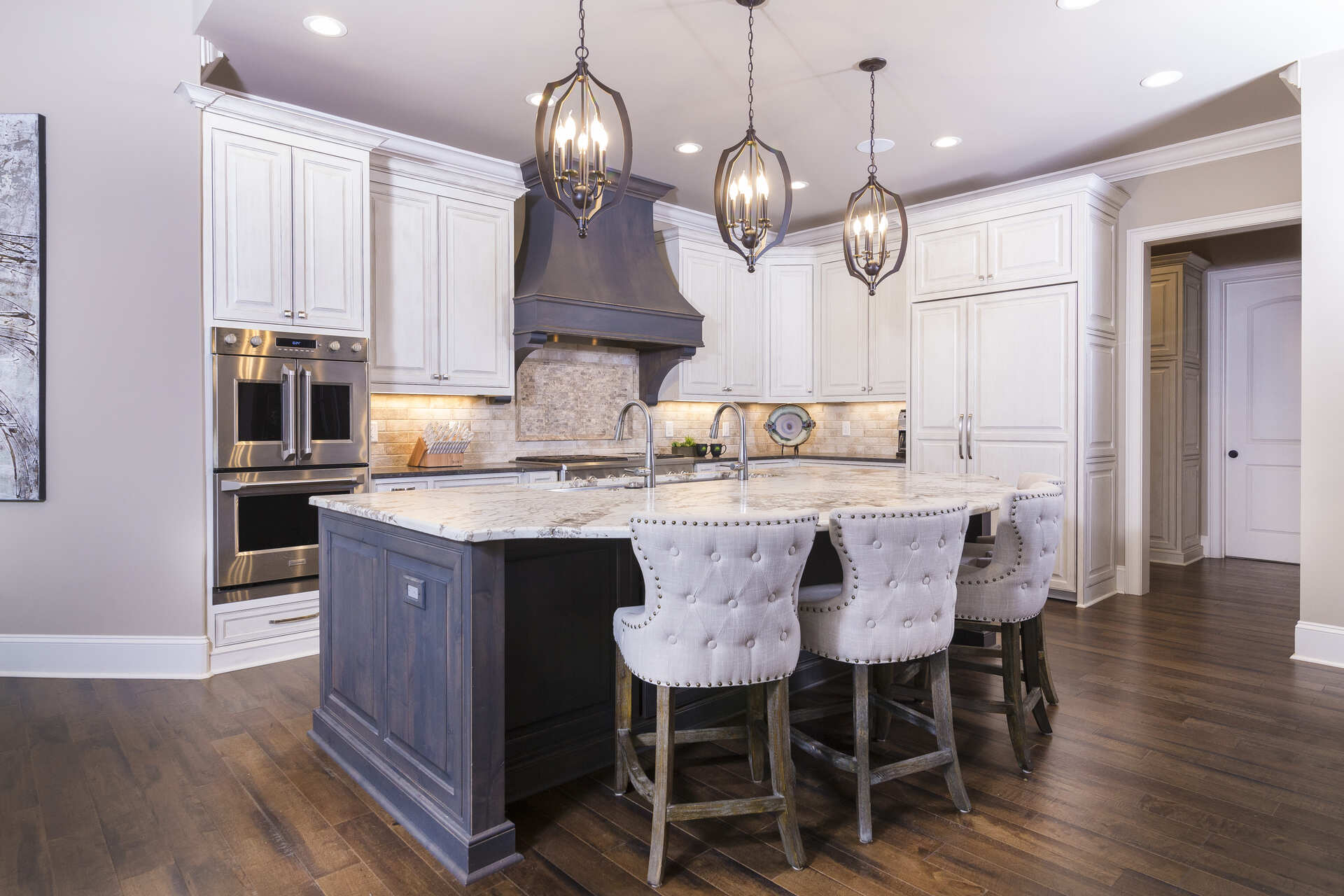 White kitchen cabinets with a brown island and large light fixtures